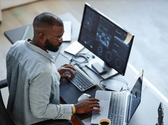 Minimal high angle view at African American software developer working with computers and data systems in office